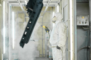 Man with spray gun painting metal in factory